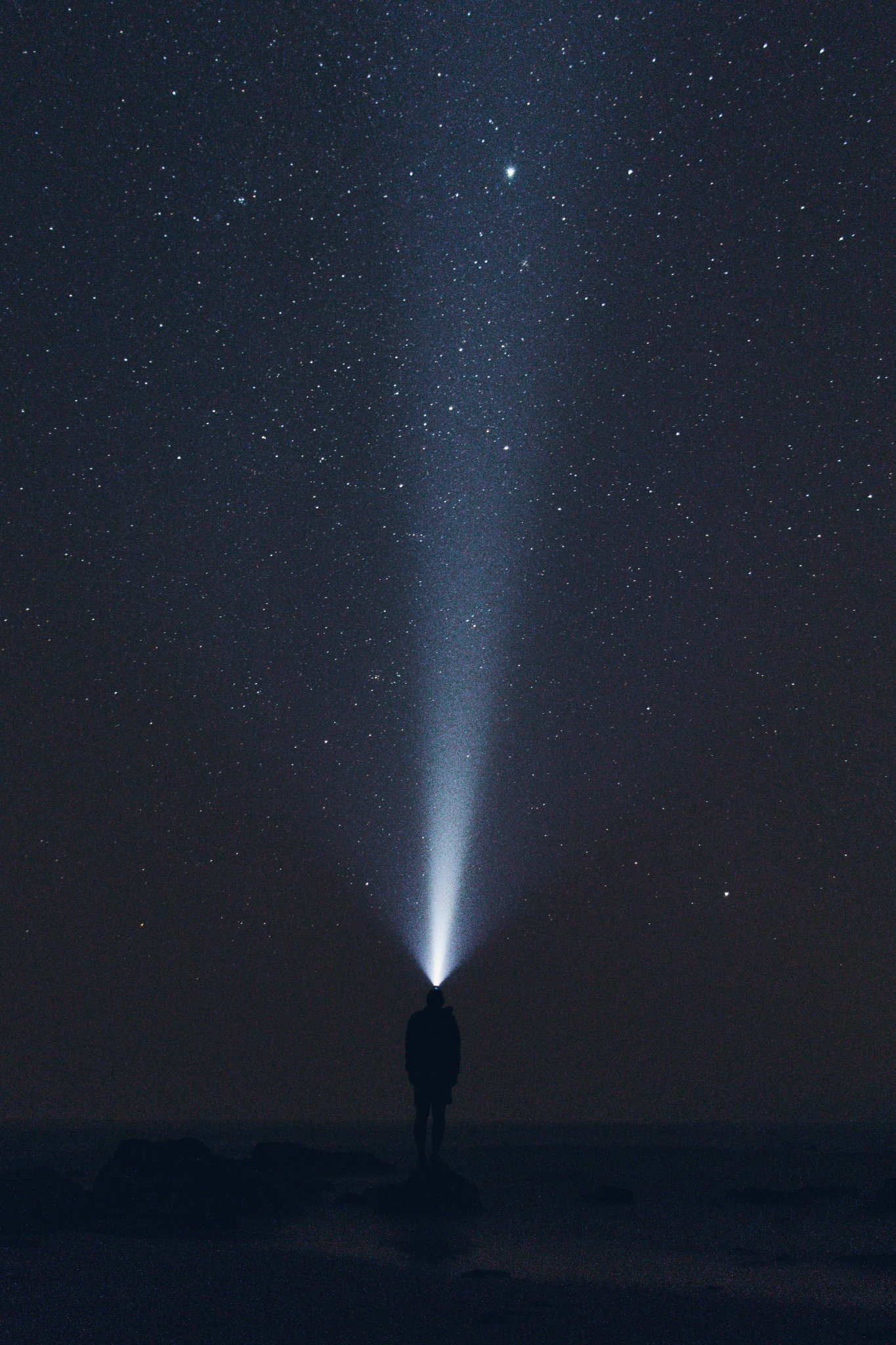 Silhouette einer Person mit leuchtender Stirnlampe unter einem Sternenhimmel