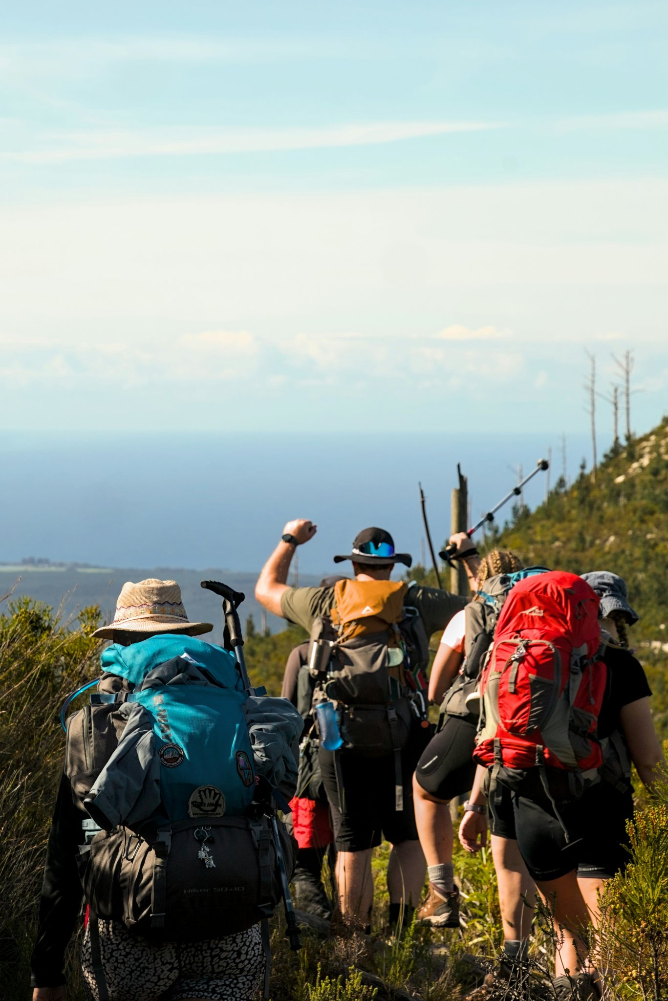 Eine Gruppe mit Rucksäcken steigt einen sonnigen Bergweg hinauf